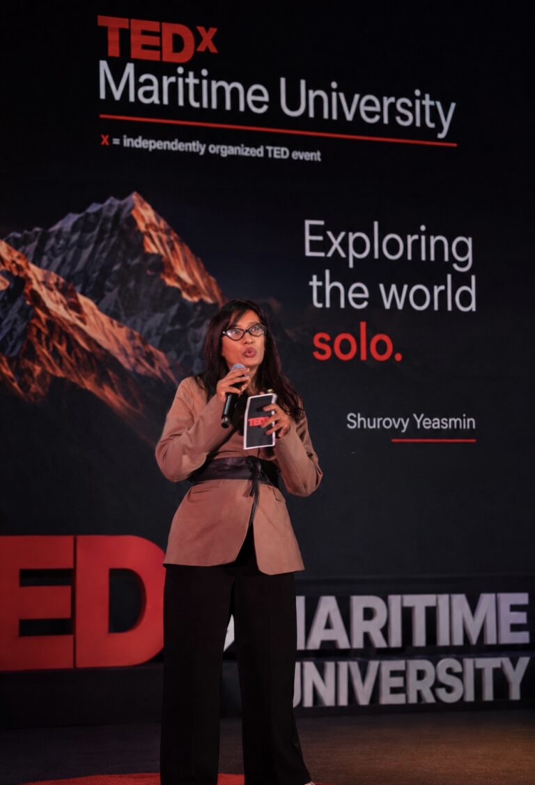 Shurovy Yeasmin speaking on stage at TEDx Bangladesh Maritime University, beside a slide reading “Exploring the world solo.”