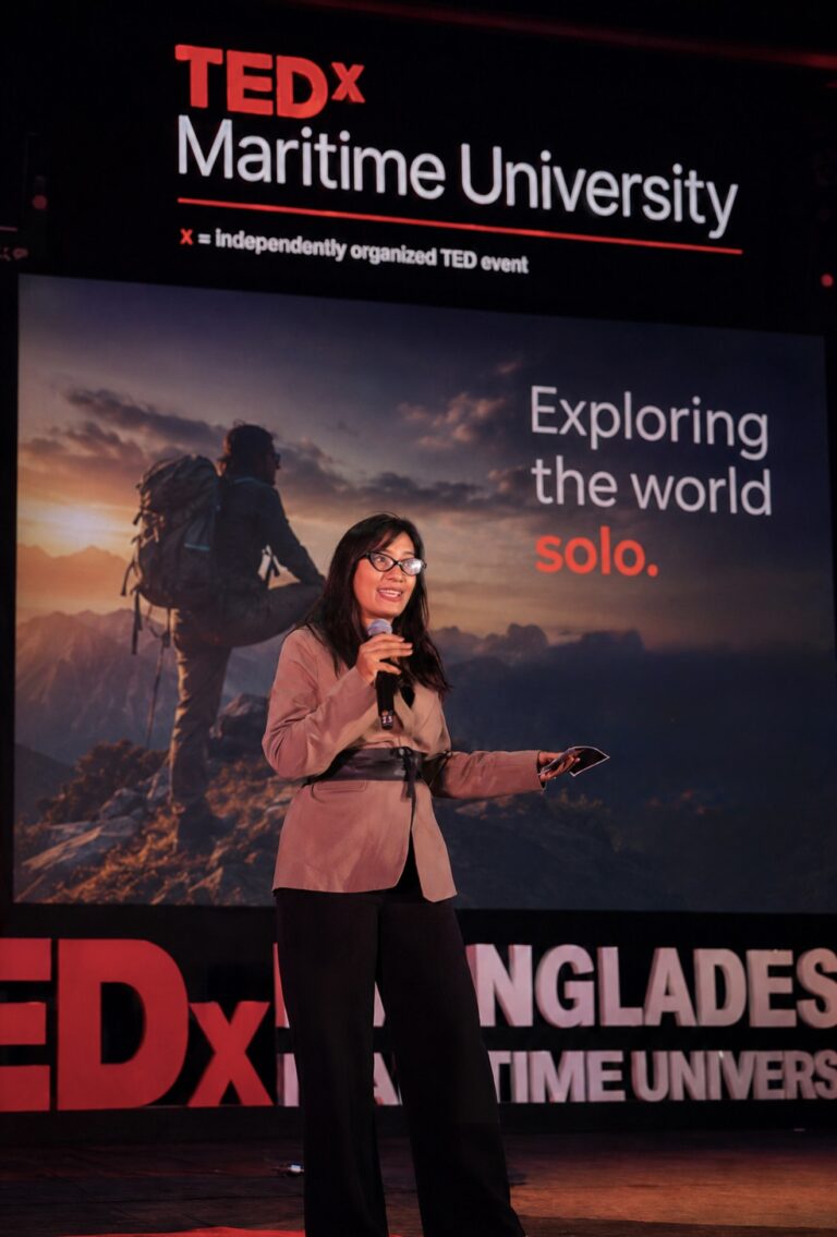Shurovy Yeasmin presenting her TEDx Bangladesh Maritime University talk in front of a slide showing a lone hiker on a mountain ridge at sunrise.
