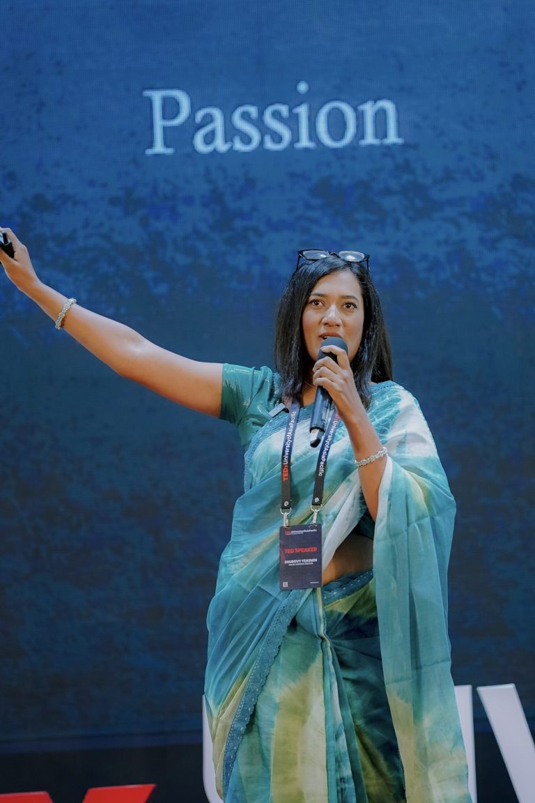 Shurovy Yeasmin on stage at TEDx University of Asia Pacific, one arm raised beside a slide titled “Passion.”